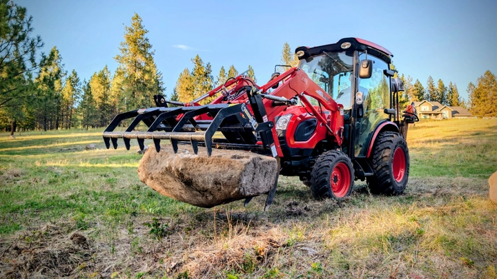 CLASP-IT mechanical grapple carrying a large boulder on a Kioti compact tractor